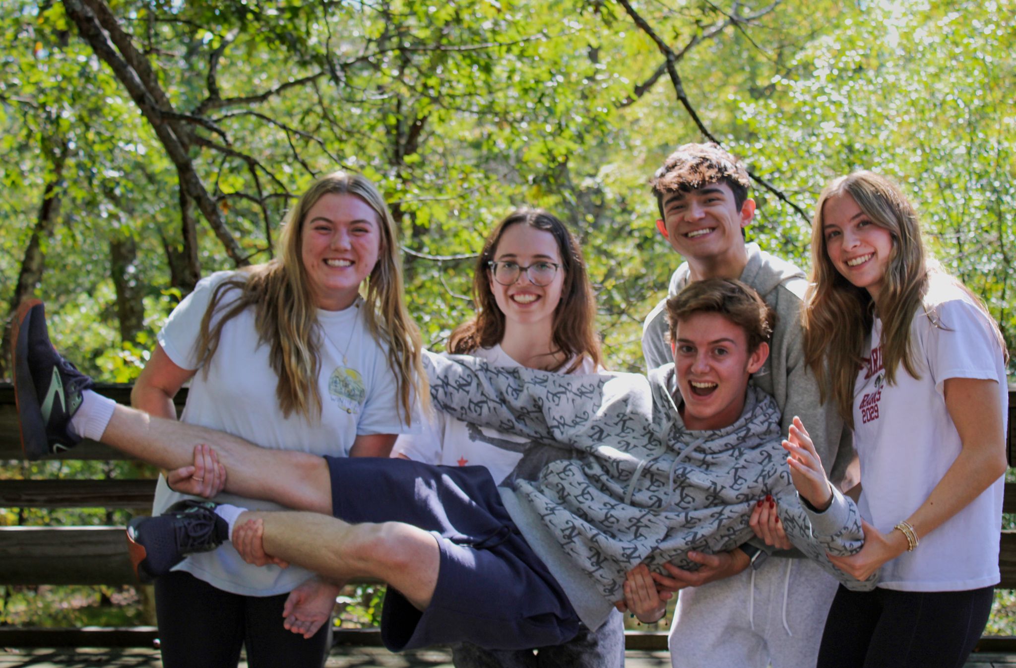 A group of students pose on retreat and hold one student up.