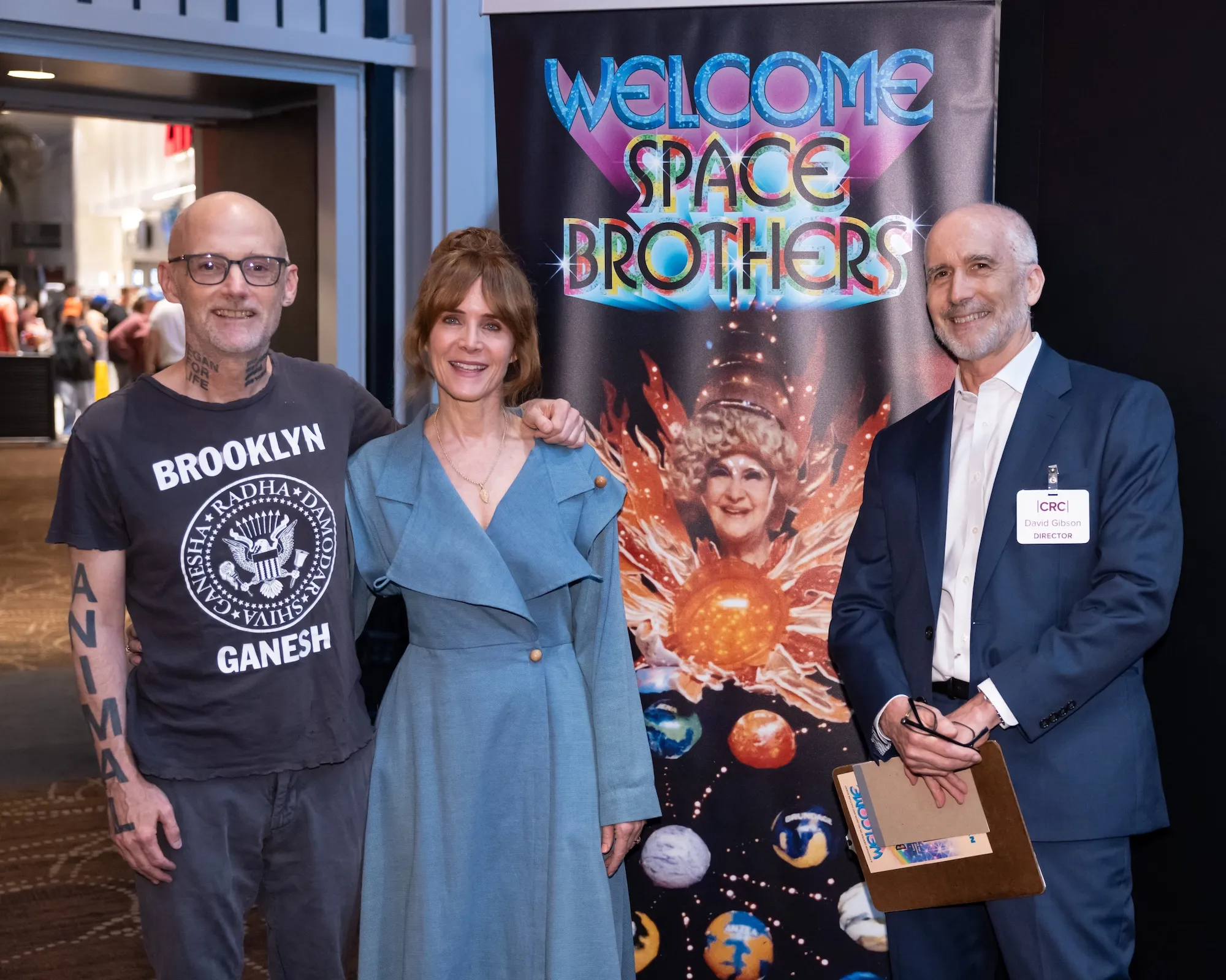 Moby, Jodi Wille, and David Gibson pose next to a banner that reads Welcome Space Brothers