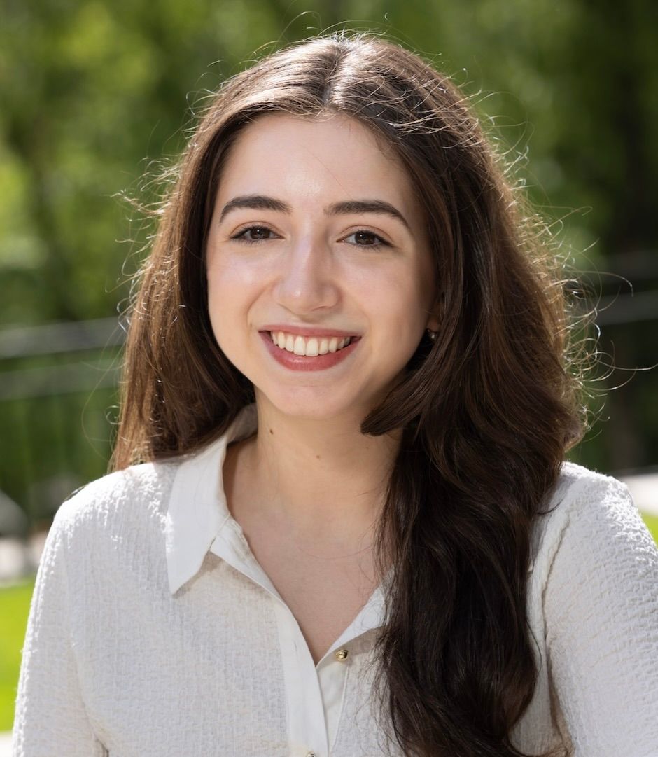 A woman smiles outside with trees in the background