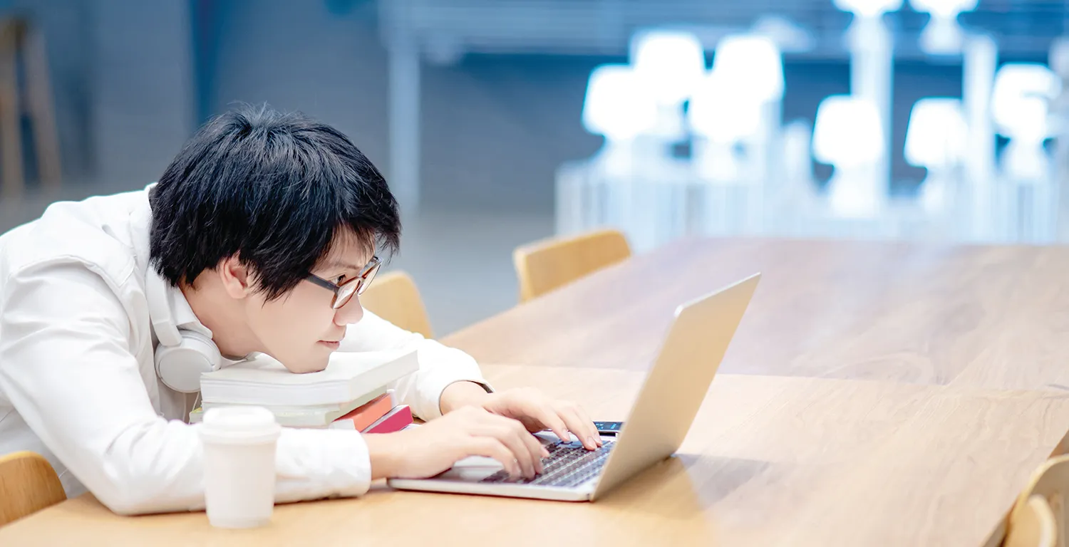Student resting on books looking at computer