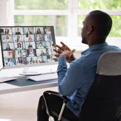 a man sits at a desk speaking to others in a virtual meeting