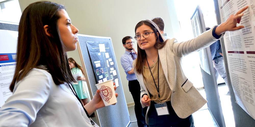 a student presents their research to an onlooker.