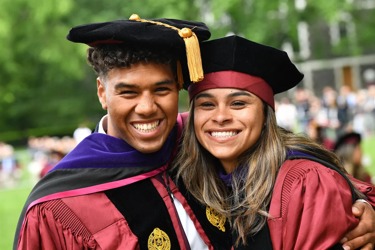 A man and a woman smiling while wearing red graduation caps and gowns.
