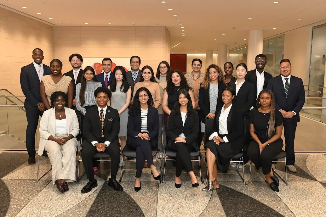 Group of students wearing suits sitting and standing inside a building with patterned floors.