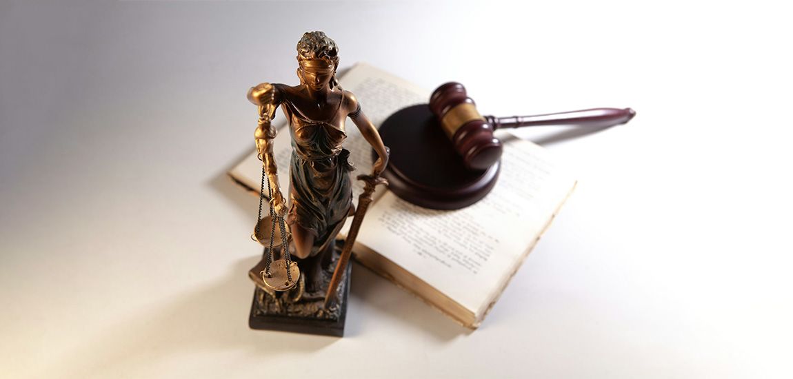 A gold statue of a blindfolded woman holding scales, in front of an open book and a gavel.